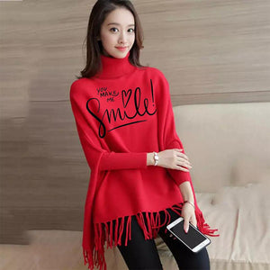 Woman wearing a red sweater with text, holding a phone, against a wooden wall.