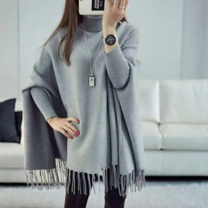 Person wearing a gray poncho with fringe in a living room setting