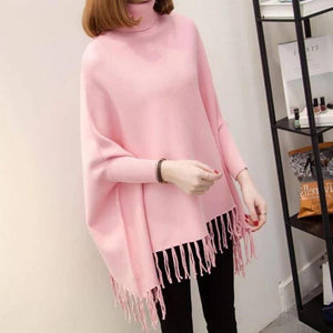 Person wearing a pink poncho with tassels indoors.