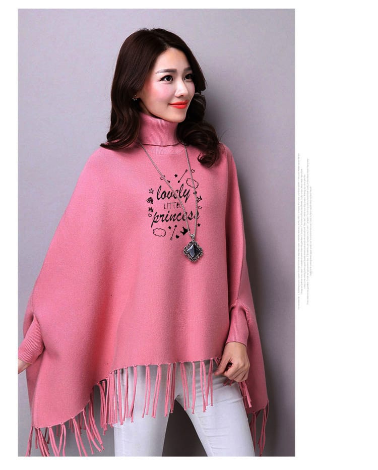 Woman wearing a pink poncho with fringe details against a plain background