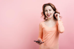 Woman in peach shirt holding a phone on a pink background